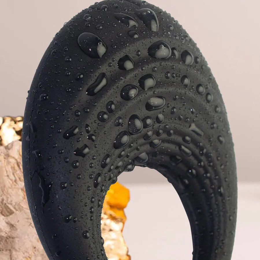 Anneau pénien vibrant noir en silicone, texturé, étanche, avec gouttelettes d'eau, fond neutre.