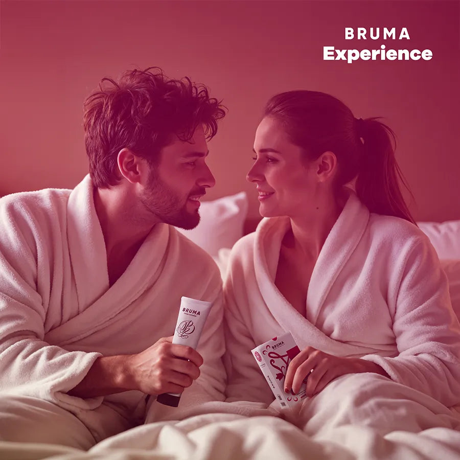 Couple souriant en peignoirs blancs avec kit BRUMA XPERIENCE rose, comprenant lubrifiant et accessoires sensuels.