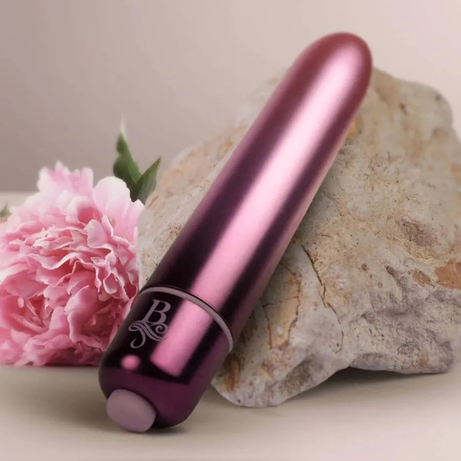 Balle vibrante rose métallique, compacte, en silicone médical, sur fond de pierre et fleur, pour stimulation précise.