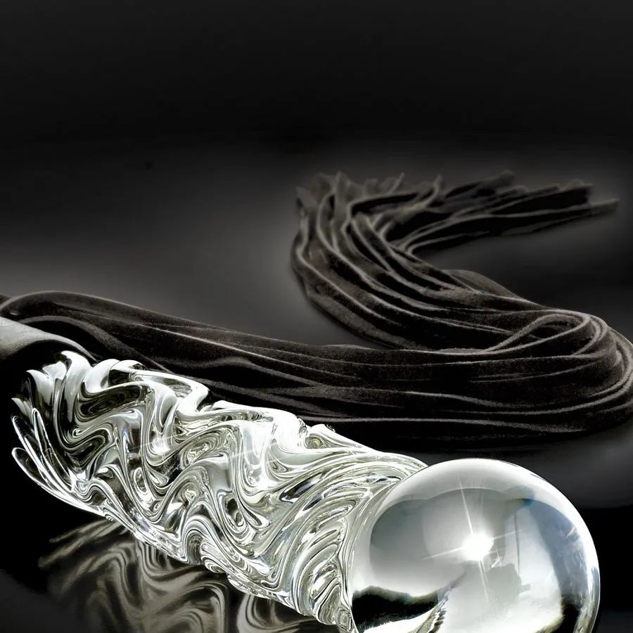 Fouet érotique en verre soufflé transparent avec manche ondulé et lanières en simili-cuir noir sur fond sombre.