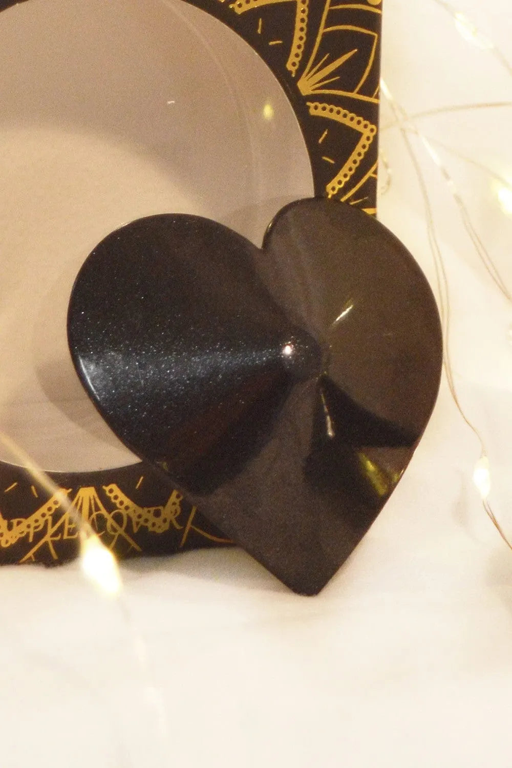Cache-téton en métal noir en forme de cœur, réutilisable, élégant, diamètre 51mm, sur fond de boîte décorative.